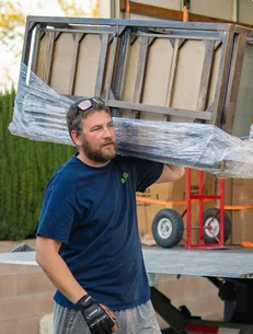 Mover carrying a shrink-wrapped chair on his shoulder beside the truck