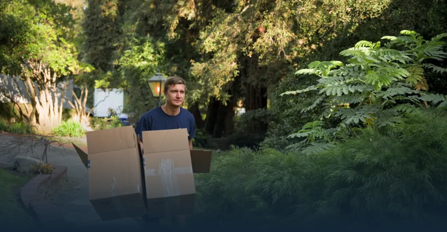 Un operario de mudanzas transporta cajas embaladas por un sendero de jardín.